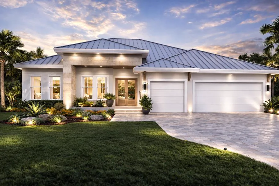 The PALMA Collection at dusk - a white home with a stone entry surround, a standing-seam metal roof and a three-car garage, lit from within