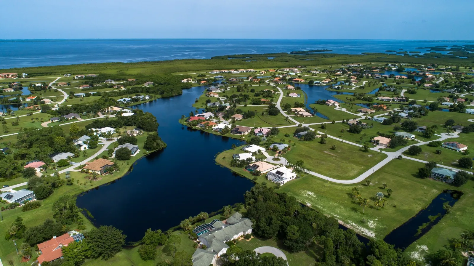 Aerial photograph of Burnt Store Lakes, Punta Gorda - homes and open lots around the freshwater lakes, with Charlotte Harbor beyond