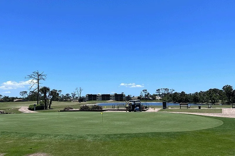 A practice putting green beside a lake near Burnt Store Lakes, Punta Gorda, with a golf cart parked by the pond