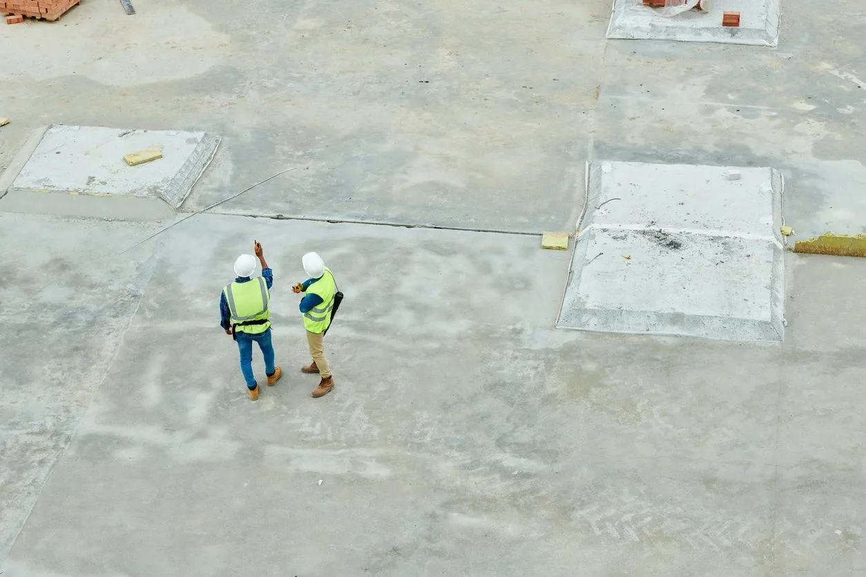Aerial view of two workers in hard hats and safety vests standing on a concrete rooftop
