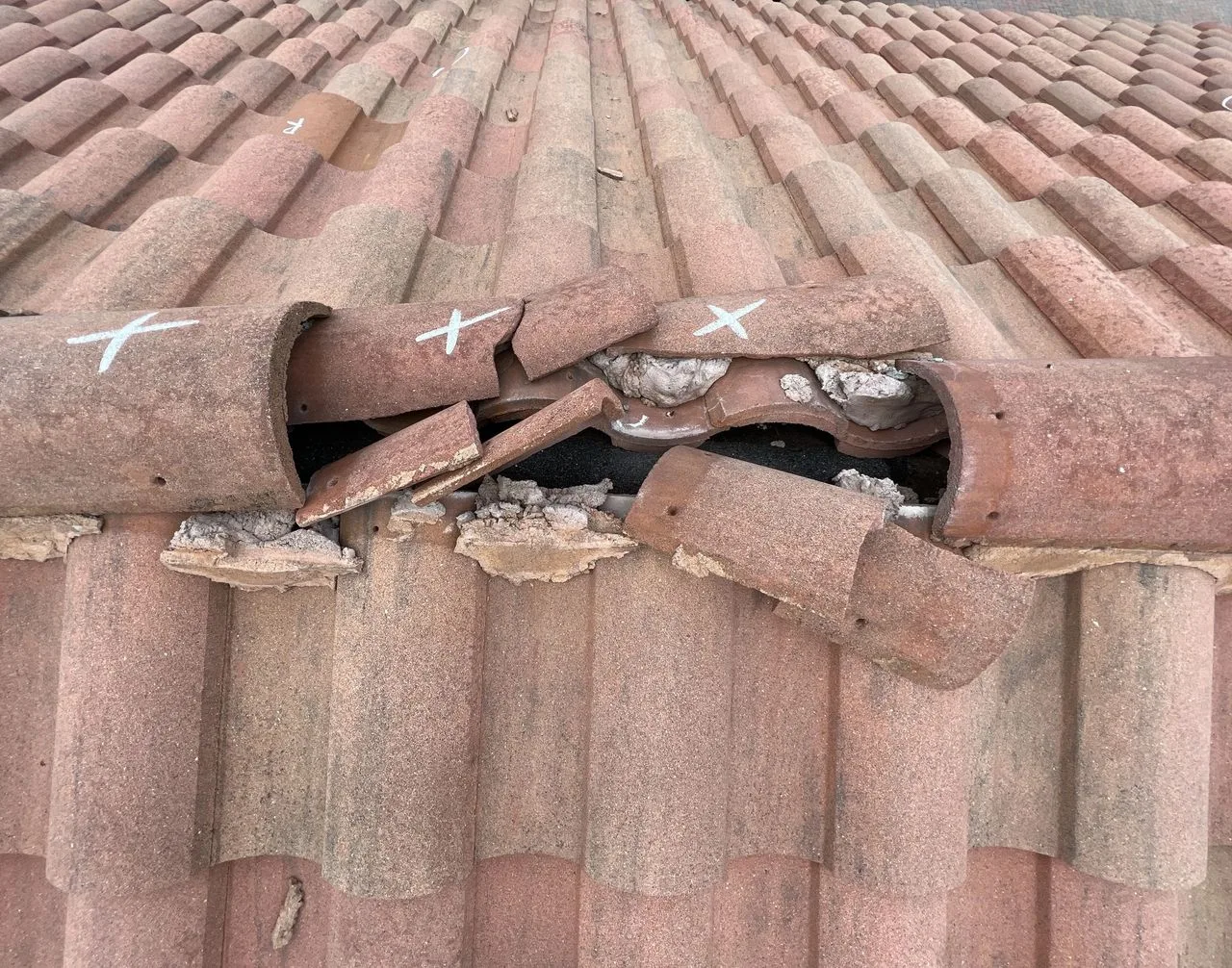 Broken clay barrel roof tiles marked with an X for replacement during a roof damage inspection