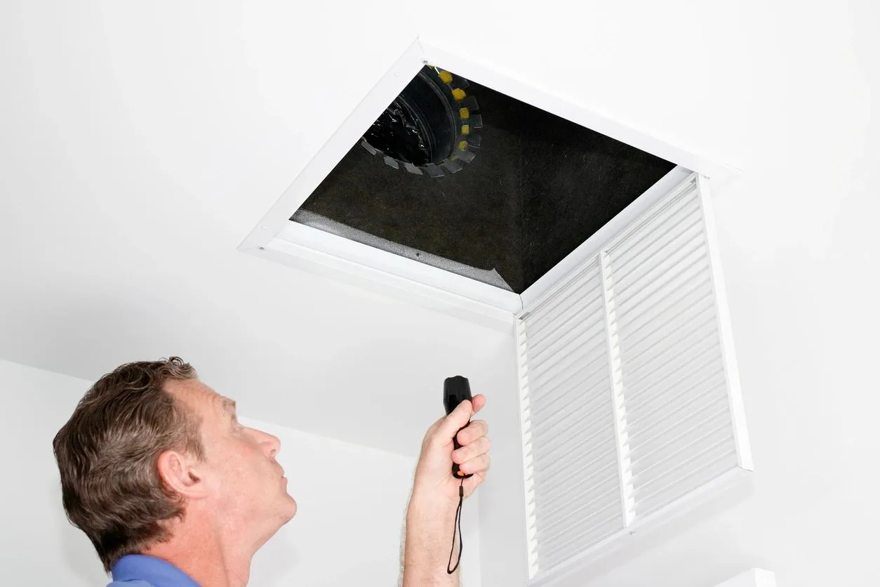 Building inspector using a flashlight to check an attic access opening and ductwork