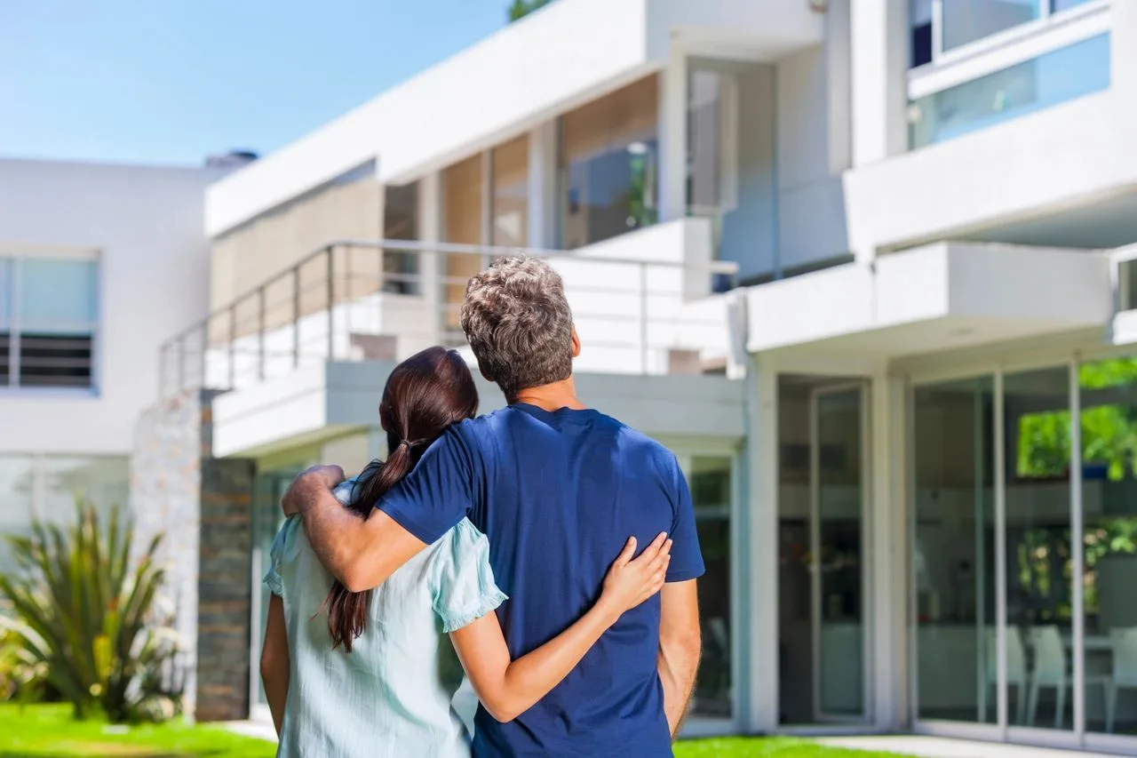 Couple with arms around each other looking up at a modern new construction home
