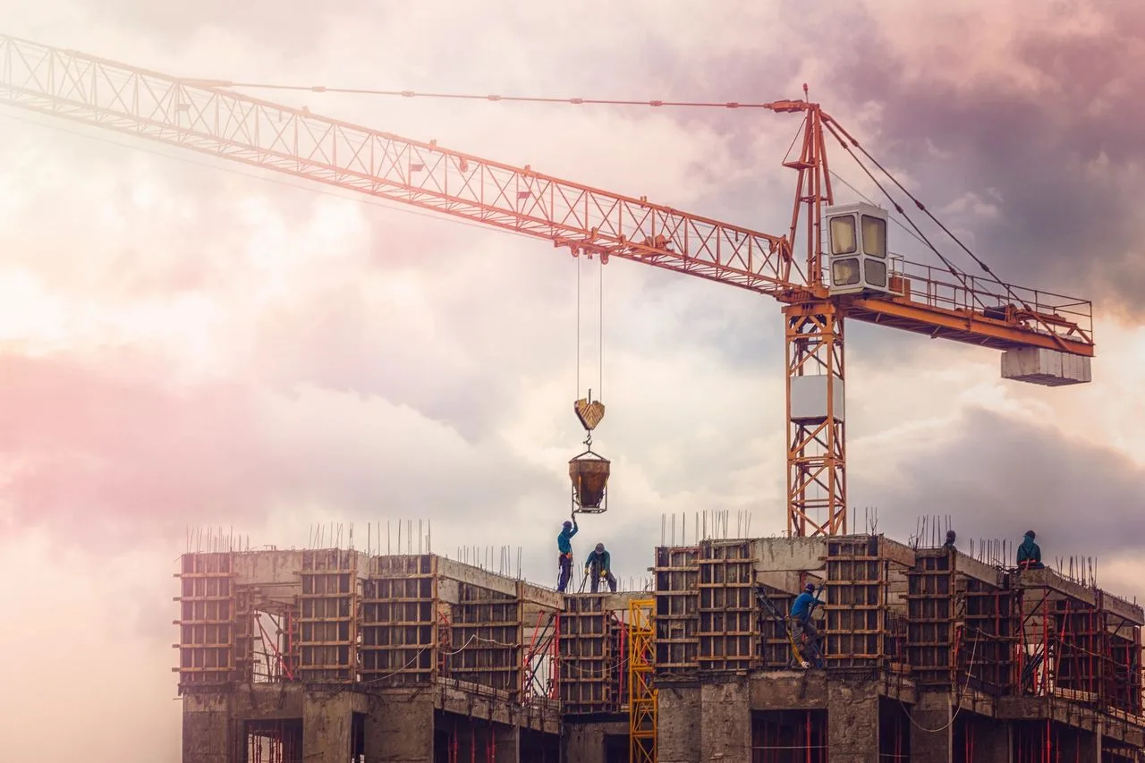 Tower crane lowering a concrete bucket to workers atop a high-rise building under construction