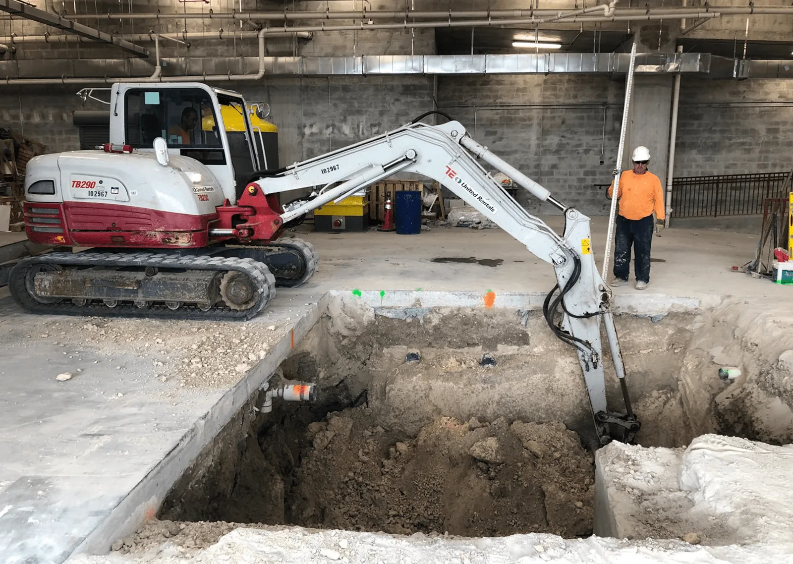 Excavator digging a foundation trench inside a parking garage under construction