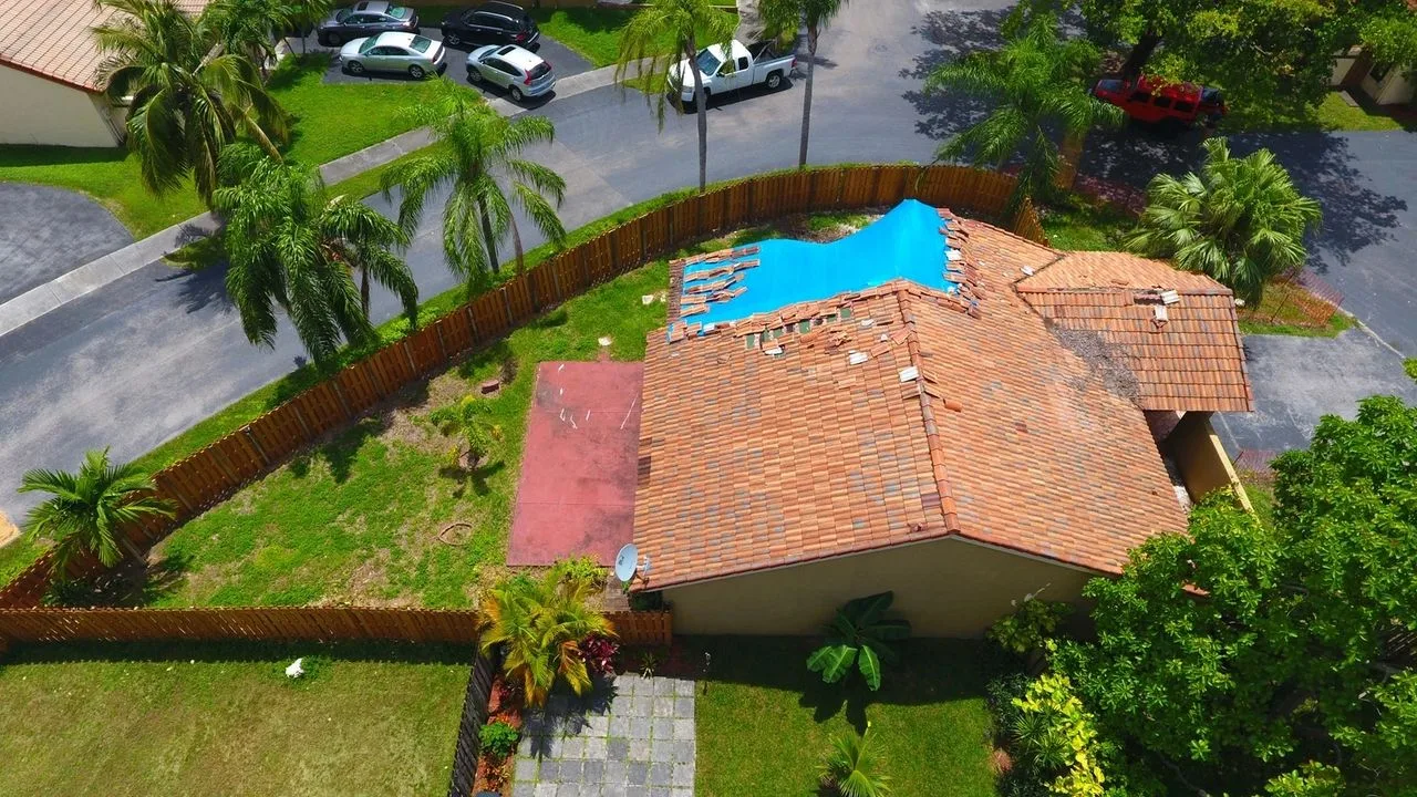 Aerial view of a Florida home’s tile roof damaged by Hurricane Irma, partly covered with a blue tarp