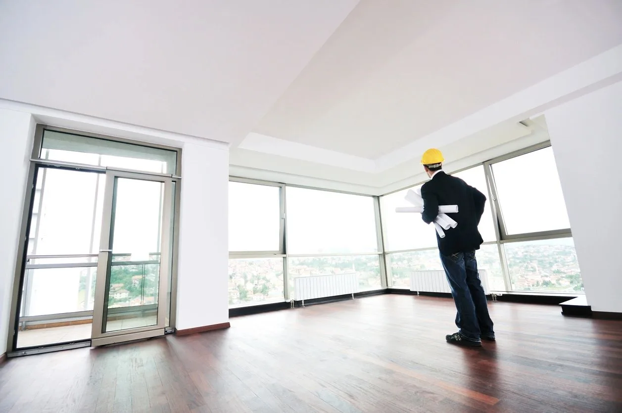 Inspector in a hard hat reviewing plans in an empty high-rise unit