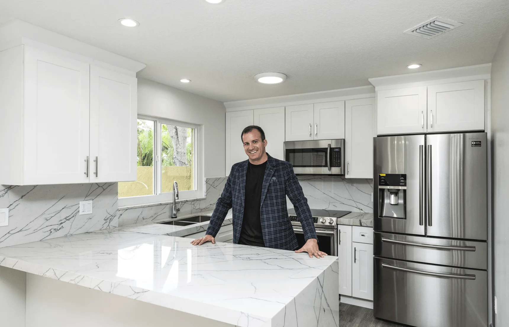 James J. Cloud standing in a renovated white kitchen with a marble island and stainless appliances