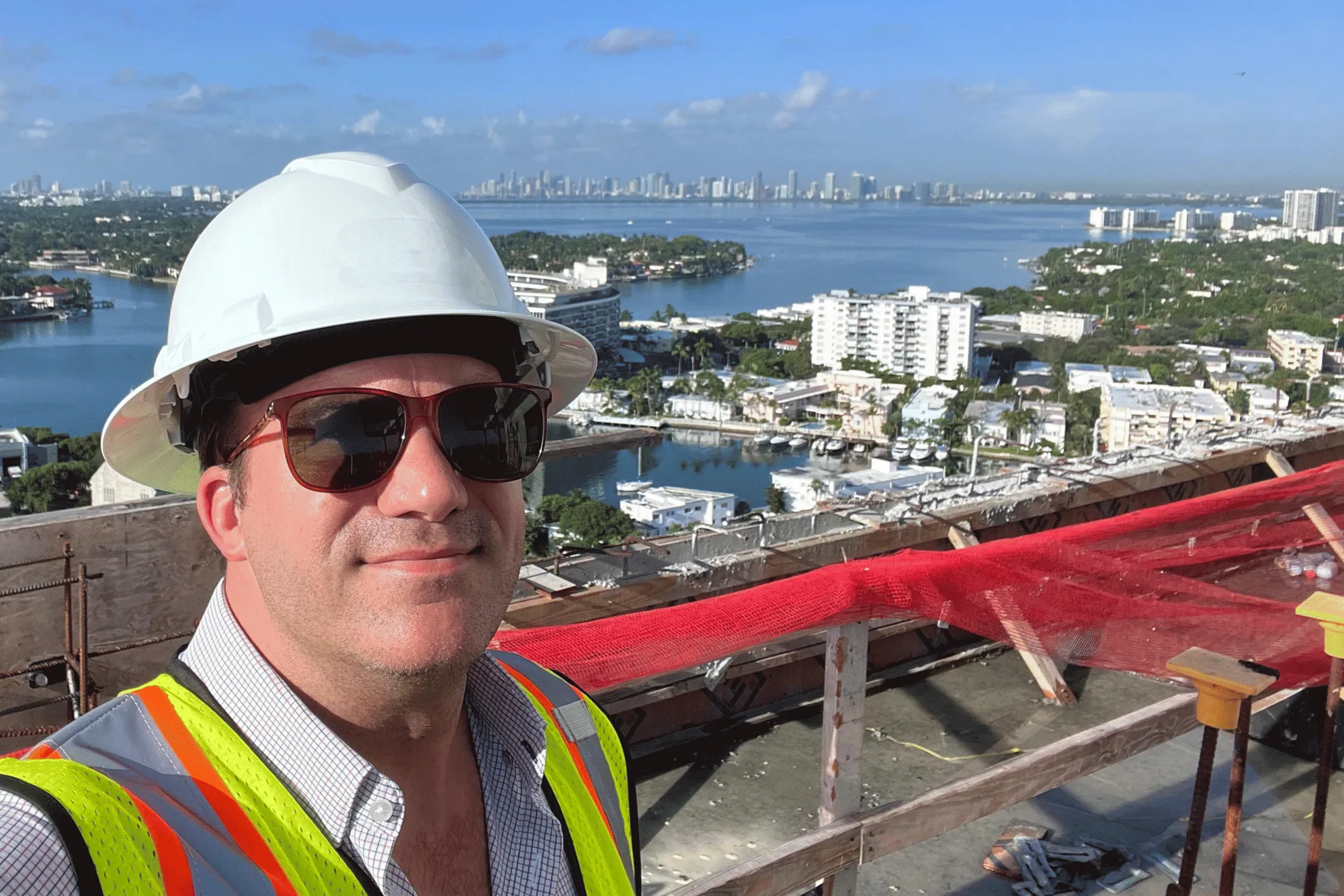 James J. Cloud in a hard hat and safety vest on a high-rise rooftop with the Miami skyline behind him
