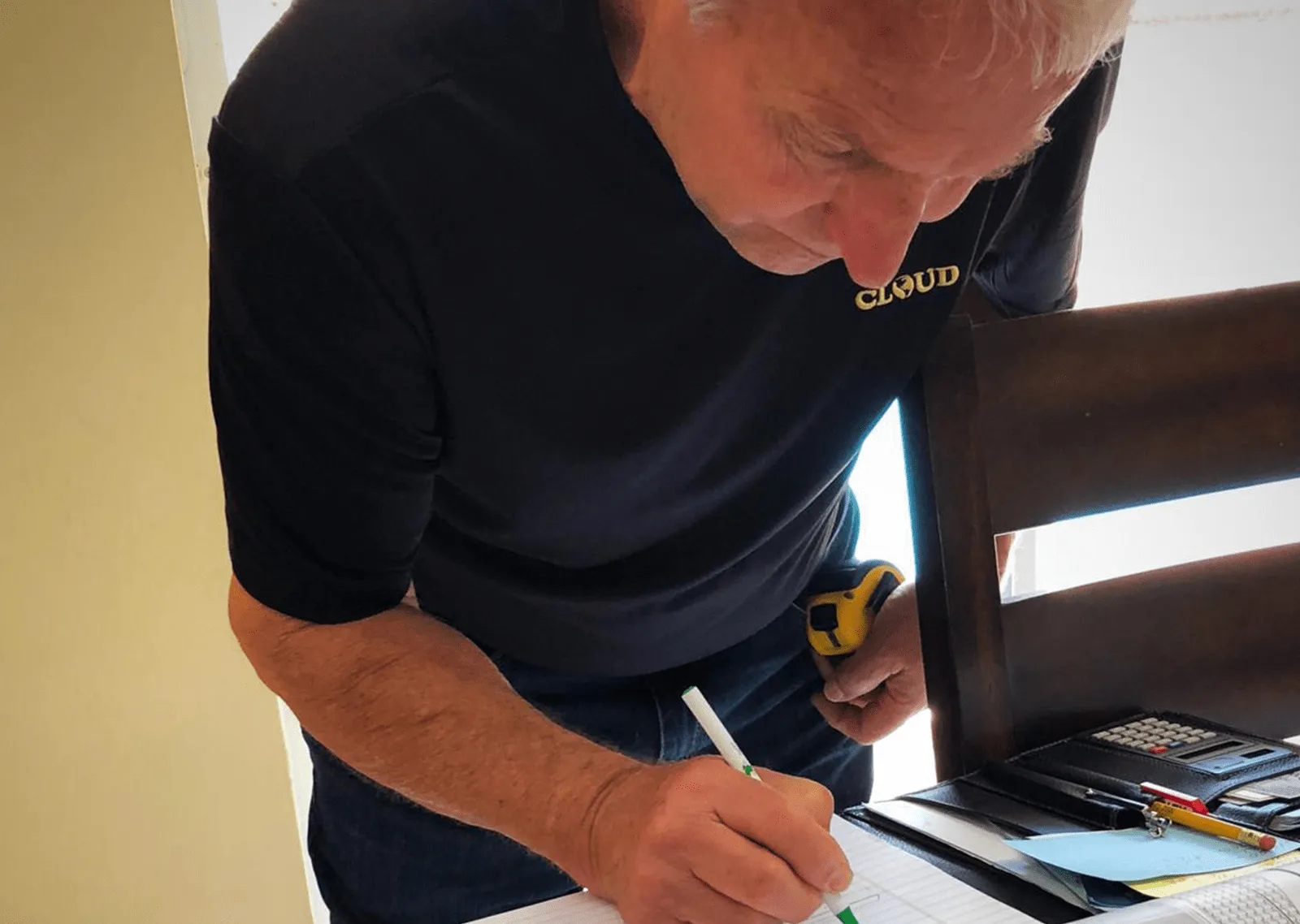 Man in a Cloud Design Build shirt writing notes at a table with a tape measure on his belt