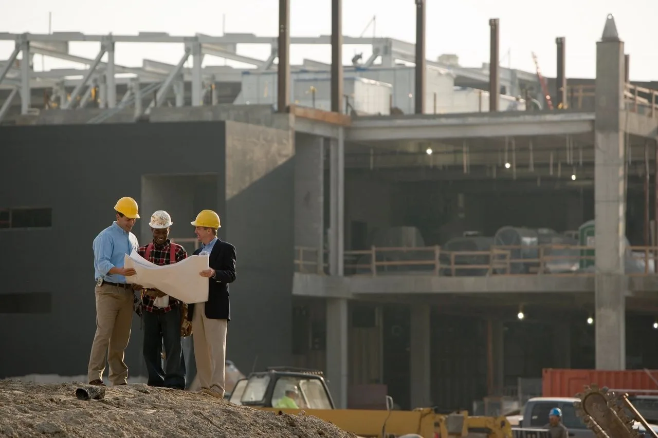 Three men in hard hats reviewing blueprints at a commercial construction site