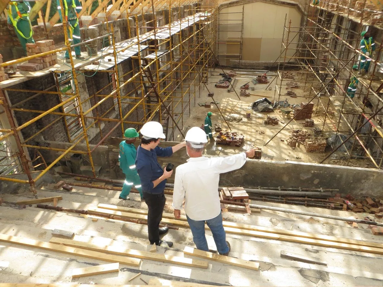 Two men overseeing work on a scaffolded building interior from above