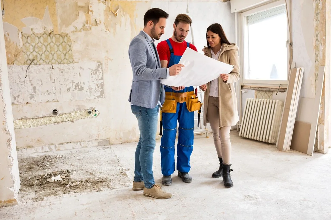 Contractor and clients reviewing renovation plans inside a stripped-down room