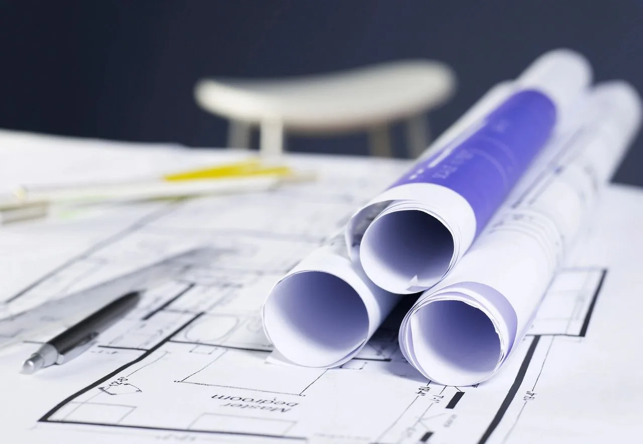 Rolled architectural house blueprints with a pencil and ruler on a desk