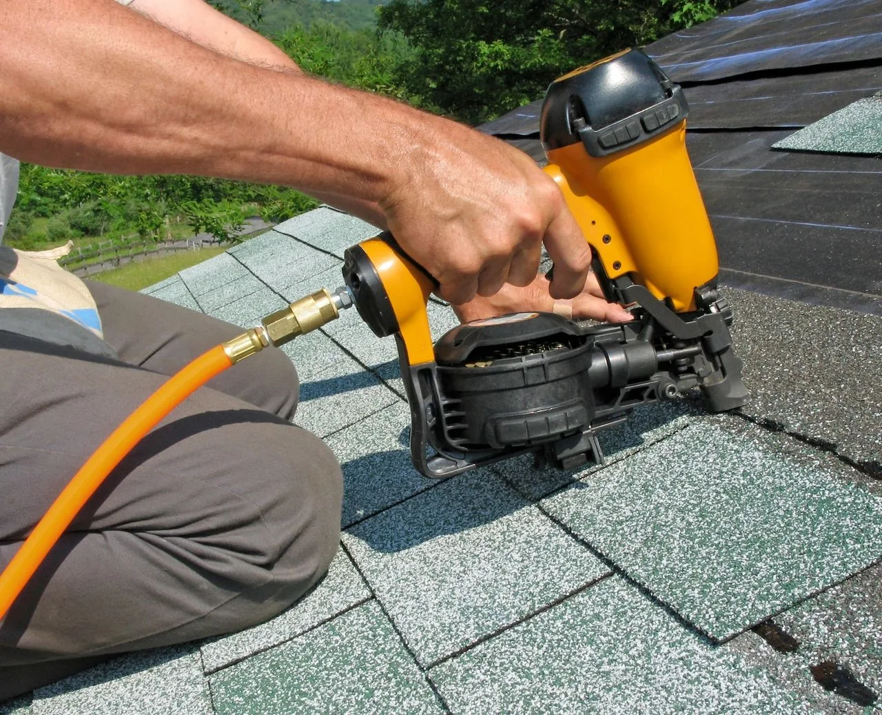 Roofer using a pneumatic nail gun to install asphalt shingles