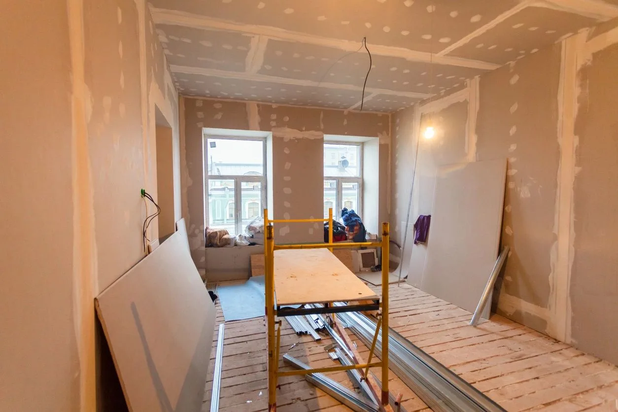 Room under renovation with taped drywall seams and a small scaffold near the windows