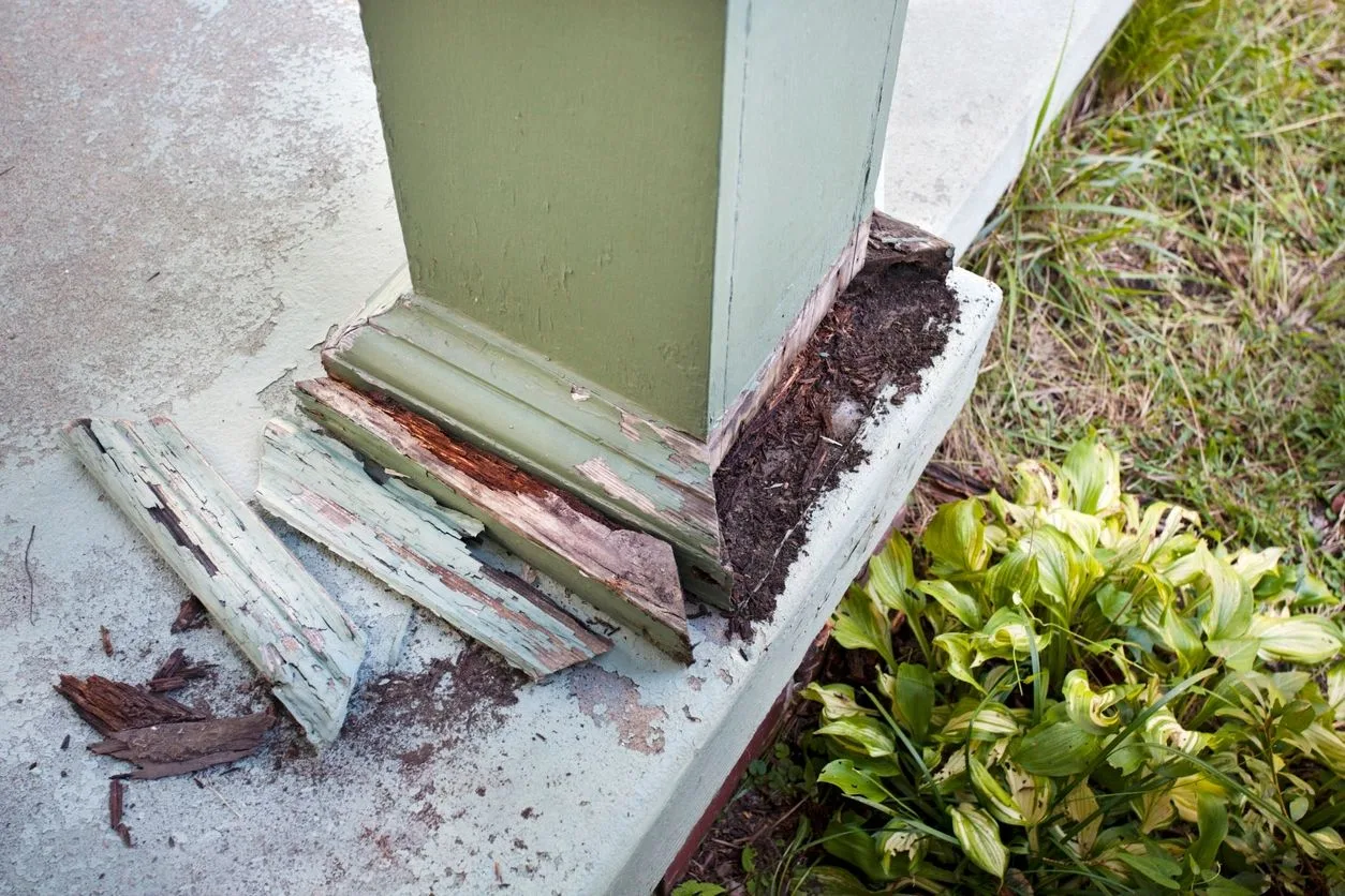 Close-up of a porch column base with rotted, peeling wood at its foundation