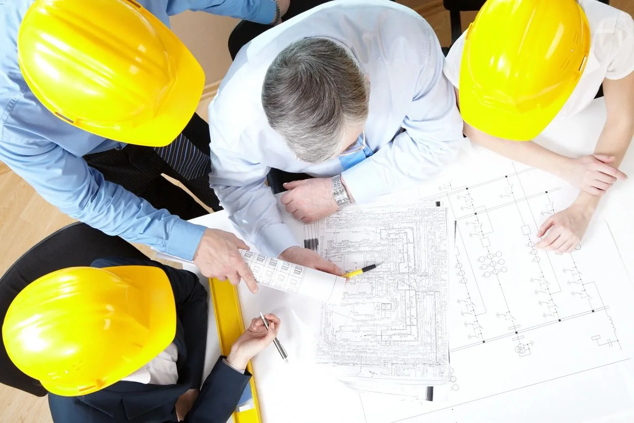 Team in hard hats reviewing an electrical blueprint together around a table