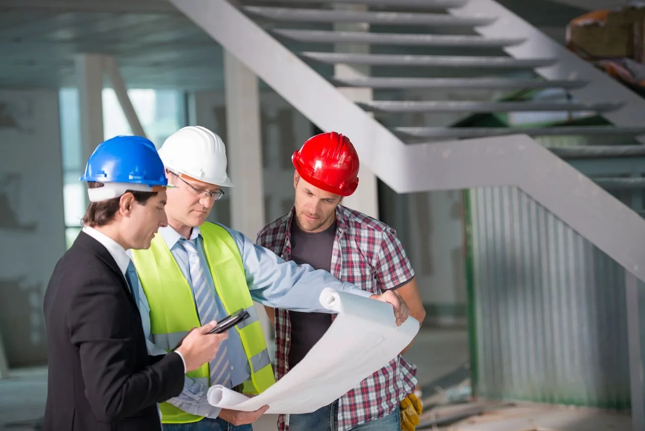 Three men in hard hats reviewing blueprints together on a commercial construction site