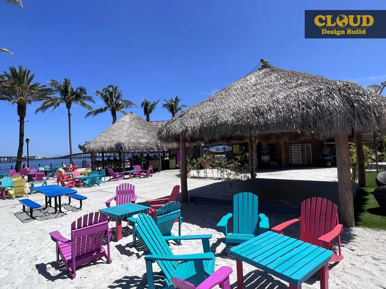 Colorful beach chairs and thatched-roof tiki huts on a waterfront patio in Punta Gorda