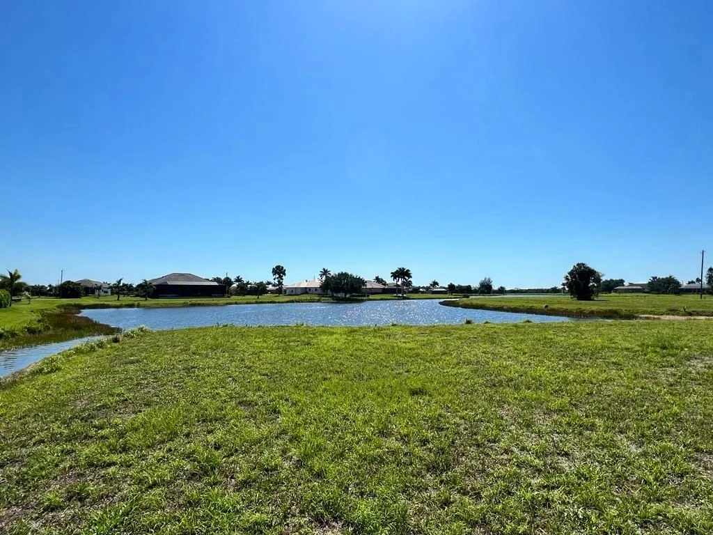 Vacant waterfront lot beside a pond with homes in the distance, ready for new construction