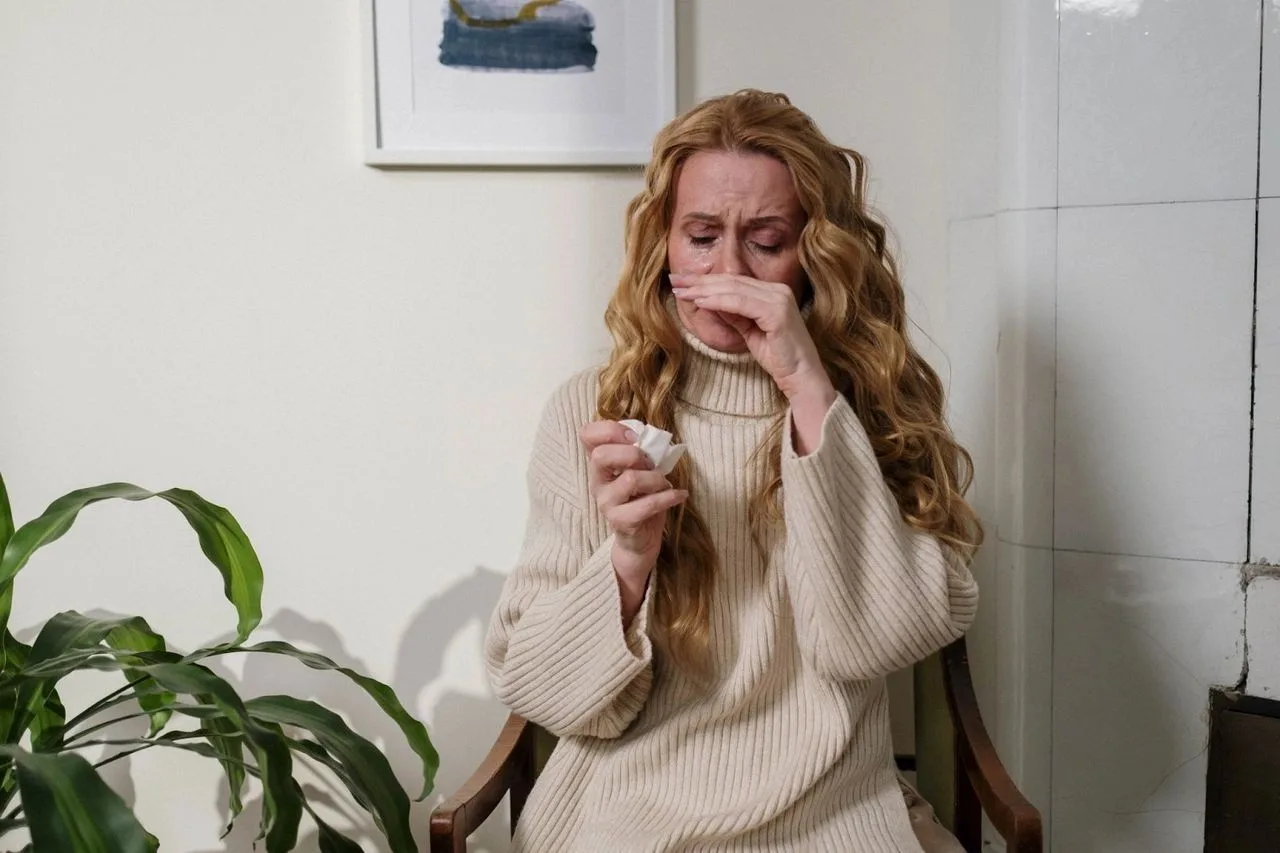 Woman covering her nose with a tissue, showing an allergic reaction at home