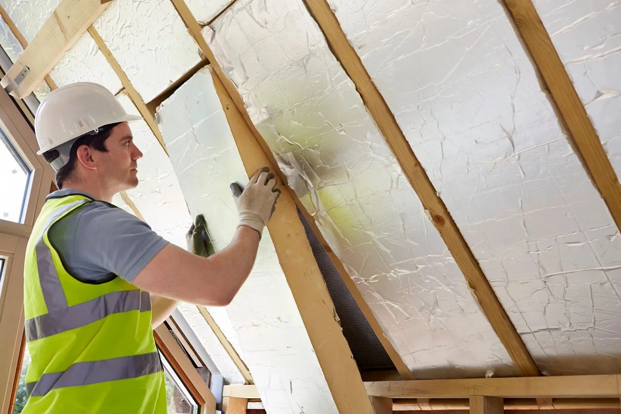 Worker installing reflective insulation between roof rafters in an attic