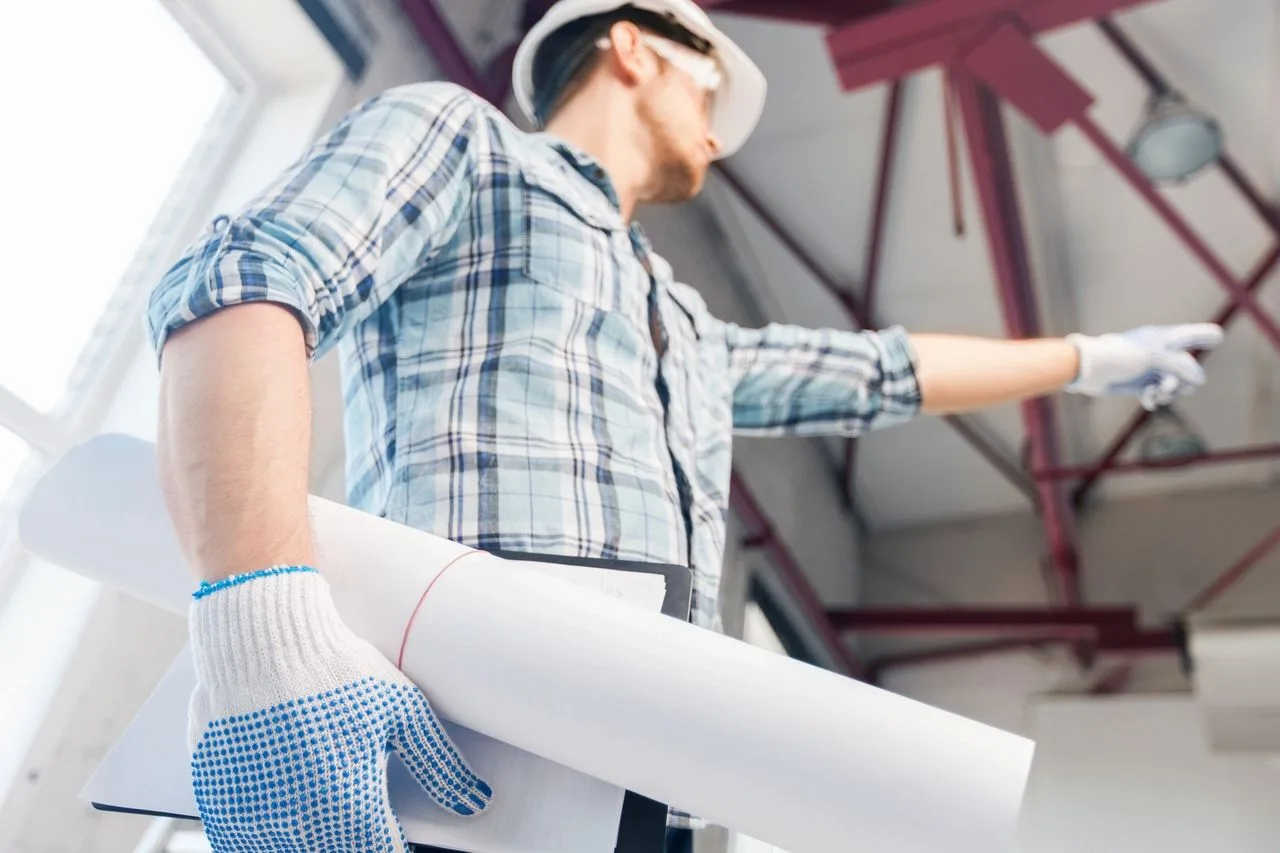 Construction worker holding rolled blueprints while pointing at overhead steel framing