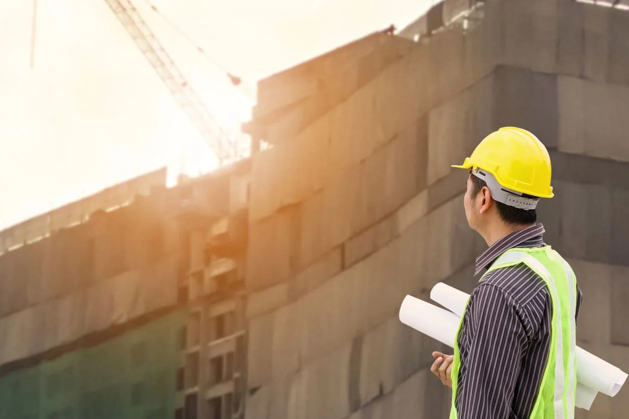 Construction professional in a hard hat looking up at a high-rise building under construction at sunset