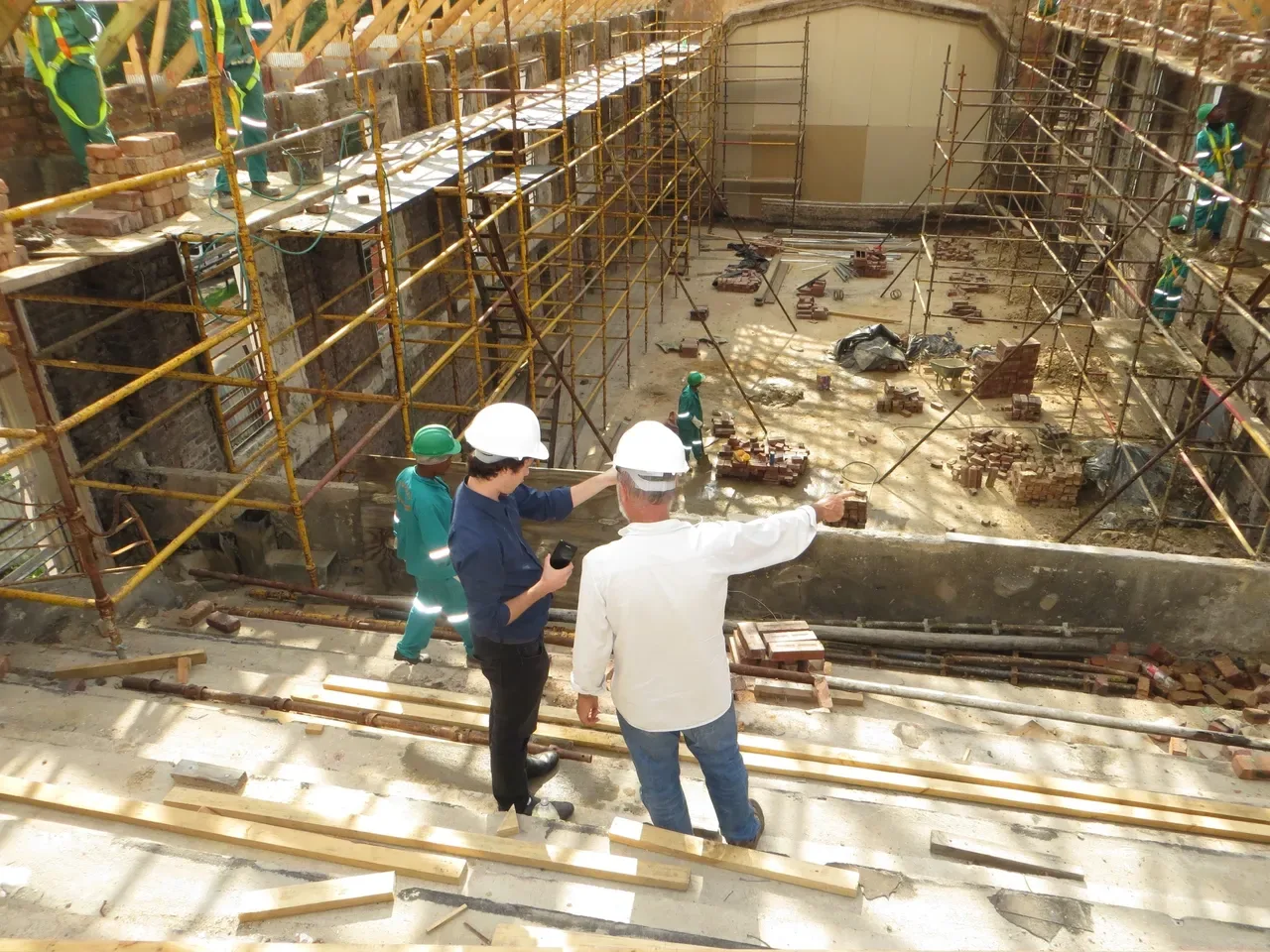 Two workers in hard hats inspecting a building interior from an elevated scaffold platform